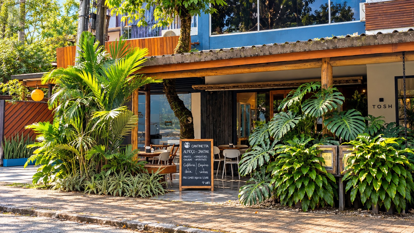 Fachada da Cantinetta com jardim tropical, mesas e lousa com o cardápio do dia